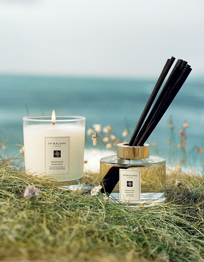 Jo Malone London Wood Sage & Sea Salt scented candle and diffuser set in coastal grass by the ocean.