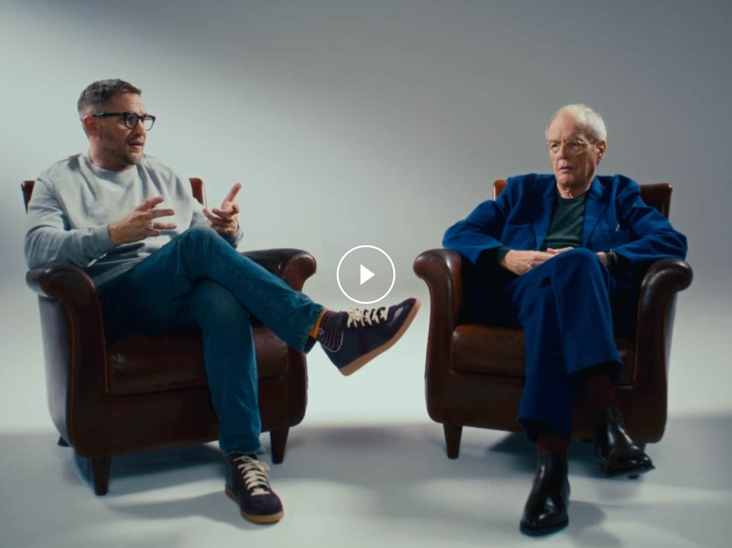 A clapperboard reveals Tom Hardy sat next to his father, against a light backdrop. He is wearing a grey jumper and glasses.