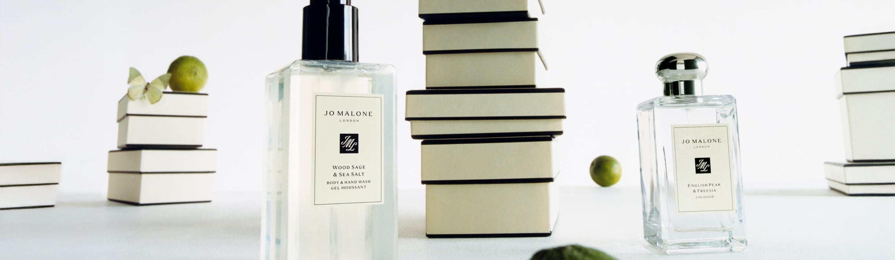 mulher sentada em uma colina, segurando caixas de presente clássicas jo malone london preto e creme